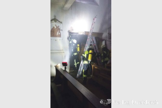 Die Feuerwehrkr&auml;fte bei L&ouml;scharbeiten am brennenden Beichtstuhl in der Pfarrkirche St. Peter und Paul. Unter Atemschutz musste die noch gl&uuml;hende Holzverkleidung aus der Wand geschnitten werden.&nbsp;
(Foto: Feuerwehr)
