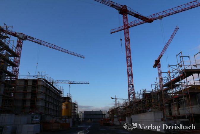 Während das Gebäude im Baufeld 1 An der Ölmühle schon seiner baldigen Fertigstellung entgegensieht, wird das übrige Baugelände noch von großen, roten Kränen und Baugerüsten beherrscht.
