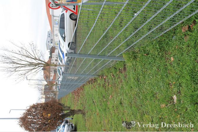 Ein Zaun trennt die Parkplätze; er muss, da es keinen Durchgang oder gar eine Durchfahrt gibt, bei einem "Seitenwechsel" umrundet werden – entweder mit dem Auto oder zu Fuß.
