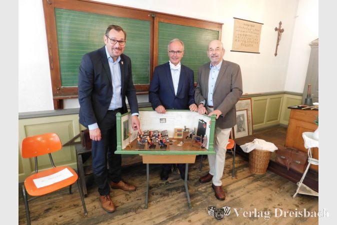Stolz präsentieren Museumsleiter Wolfgang Janecke, Bürgermeister Christian Seitz und der ehemalige Schuldezernent Wolfgang Kollmeier die historische Puppenschule aus dem Hause Rothschild.