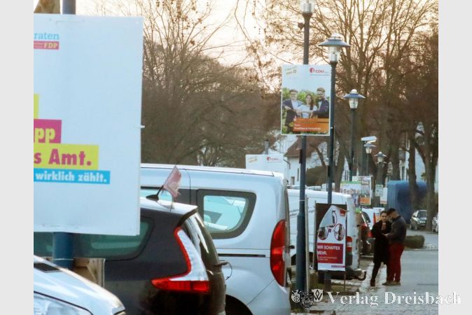 Normalerweise würden wir an dieser Stelle auf eine konfrontative, diskussionsfreudige, vielfältigen, bunte und hoffentlich dennoch faire Wahlkampfzeit im Spätwinter 2021 zurückblicken, denn am 14. März wurden in Hessen die Kommunalparlamente neu gewählt. Das Werben der Parteien um die Gunst der Wählerinnen und Wählern fand diesmal aber vor allem über die Medienschiene statt: Flyer, wie hier am Adenauer-Ufer zu sehen jede Menge Plakate an den Laternenpfählen, Zeitungsanzeigen – aber keine öffentlichen Wahlveranstaltungen oder Kundgebungen, und selbst den klassischen Wahlkampfstand auf dem Wochenmarkt gab es diesmal kaum. Der Inzidenzwert lag in der heißen Phase des Wahlkampfs bei Werten, die wir aktuell gerne wieder hätten, im Landkreis zwischen 50 und 80. Die Unsicherheit durch die Coronakrise ließ aber keine Planungen für Begegnungen zwischen Kandidierenden und Wahlvolk zu. Die Parteien, die es versuchten, thematische Treffen per Online-Wahlstände anzubieten machten die Erfahrung, dass solche Alternativangebote im Netz keine gute Resonanz über den engen eigenen Kreis hinaus fanden. Die Wahl selbst verlief problemlos, zumal ein großer Anteil der Bürgerinnen und Bürger dem Wunsch der Verwaltung nachkam, diesmal per Briefwahl mitzumachen. Bei einer allerdings erneut niedrigen Gesamtbeteiligung von nur 51,2 Prozent (2016: 51,0) verpassten die Briefwähler/innen die Zweidrittelmehrheit nur knapp (64, 5 Prozent). Werte, von denen die fünf angetretenen Fraktionen – das unveränderte Angebot zur vorigen Wahl – nur träumen konnten.