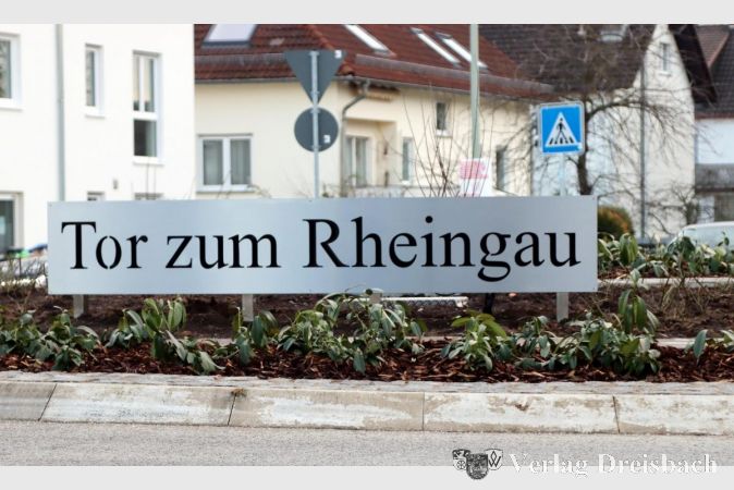 Viele Gedanken machten sich die Wickerer über die Gestaltung ihres Verkehrskreisels. So ein Ding macht stolz, zeigt es doch, dass auch ein so kleiner Stadtteil eine derart wichtige Verbindungsstraße besitzen kann, dass die Stadt sogar Fördermittel zum Umbau der Kreuzung Kirschgartenstraße/Flörsheimer Straße zuerkannt bekam. Die Bauweise eines Kreisels bringt es aber auch mit sich, dass in seiner Mitte eine gar nicht mal so kleine, kreisrunde Insel entsteht, die von den Fahrzeugen konsequent umkurvt wird, wenn es gut läuft. Das wiederum ermöglicht nahezu unbegrenzte Möglichkeiten, um den täglich tausendfach gesehenen Knotenpunkt attraktiv und werbewirksam zu gestalten. Im Entwurfsprozess lernte die Stadt dann zwar, dass die Genehmigungsbehörden dann doch die eine oder andere Grenzen setzten, vor allem, was die Höge der Aufbauten und Bepflanzung betrifft. Im Februar, mit nur leichter Verzögerung gegenüber den Planungen, war die bauliche Neugestaltung des Kreisels dann aber abgeschlossen. Das zunächst noch verhüllte Schild, das den Verkehrsteilnehmern entgegenprankt, die aus Richtung Weilbach in den Kreisel einfahren, verkündet den Beinamen Wickers als „Tor zum Rheingau“, das beleuchtete „W“-Logo (Wappen) befindet sich auf der anderen Seite. Die vollständige Bepflanzung erfolgte erst nach der Winterzeit und bliebe nicht ohne Kritik.