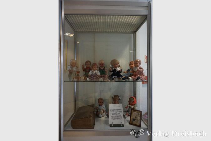 Links im unteren Regal die Bibel „Biblia Sacra Vulgata“, rechts ein Foto von Hildegard Becker als Kind, mit einer Puppe im Arm.