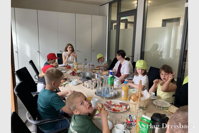 Acht Ferienspielkinder beim Frühstück im Sitzungssaal des Rathauses.
