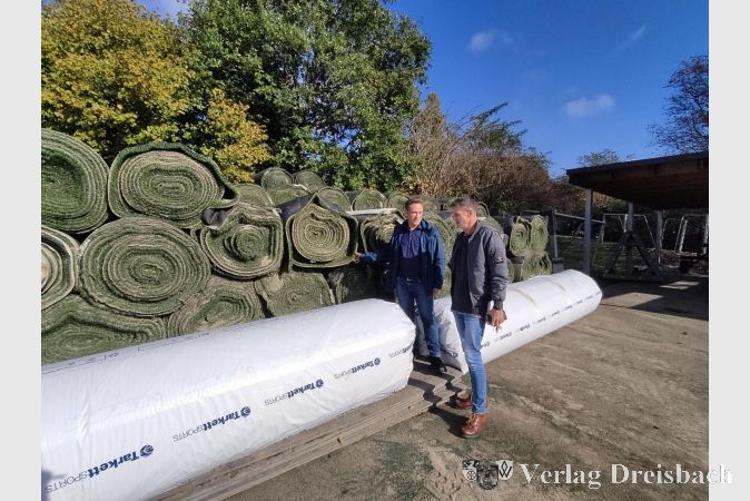 Hier sieht man im hinteren Bereich den alten Kunstrasen, der aufgrund von Sand und Mikroplastik speziell entsorgt werden muss, und im vorderen Bereich einige neue Rollen noch weiß eingepackt. Die Verlegung hat am Mittwoch begonnen.