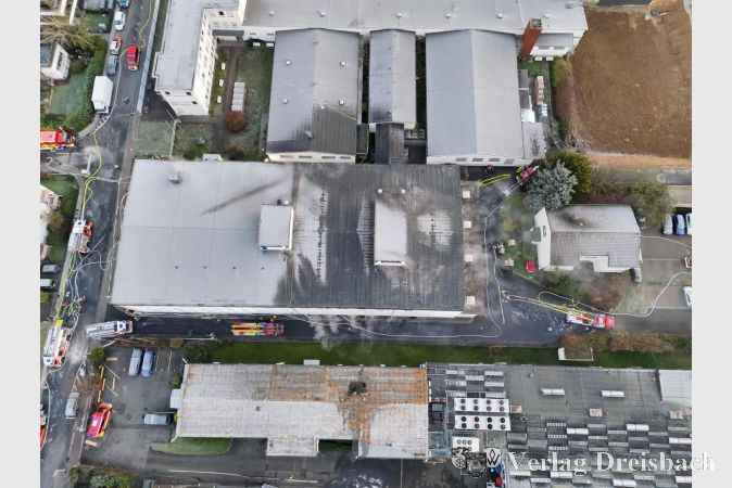 Einsatzkräfte der Feuerwehr bei den Nachlöscharbeiten an dem betroffenen Gewerbeobjekt. Der Einsatzbereich ist teilweise mit Löschschaum abgedeckt, Fahrzeuge und Geräte stehen rund um das Gebäude bereit.