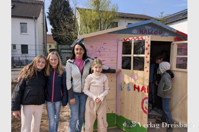 Foto: nab
Farbe am Eingang: Schulleiterin Annette Spichal präsentiert gemeinsam mit Kindern die bunt bemalte Holzhütte, die künftig als Ausleihstation für Pausenspielzeuge dient.